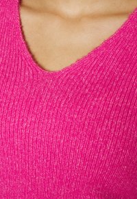Figurbetonter rosa V-Ausschnitt-Pullover mit geripptem Textur. Der Stoff wirkt weich und ist dicht gewebt, mit Farbvariationen.