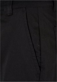 Pantalon noir en tissu robuste, avec une texture lisse, un design ajusté, des poches latérales et des détails de couture subtils.