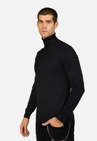 Maglione a collo alto nero realizzato in materiale a coste, design aderente, maniche lunghe, texture liscia, abbinato a pantaloni scuri e accessori.