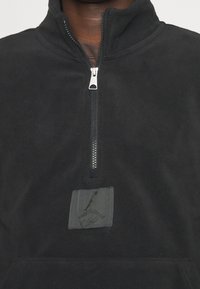 Pullover in pile nero con design a zip parziale, caratterizzato da un pannello testurizzato con un logo. Tessuto liscio e dettagli di cucitura discreti.