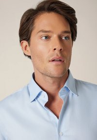 Jasnoniebieska koszula na guziki z teksturowanej tkaniny z kołnierzykiem typu kent. Posiada białe guziki i dopasowany krój.