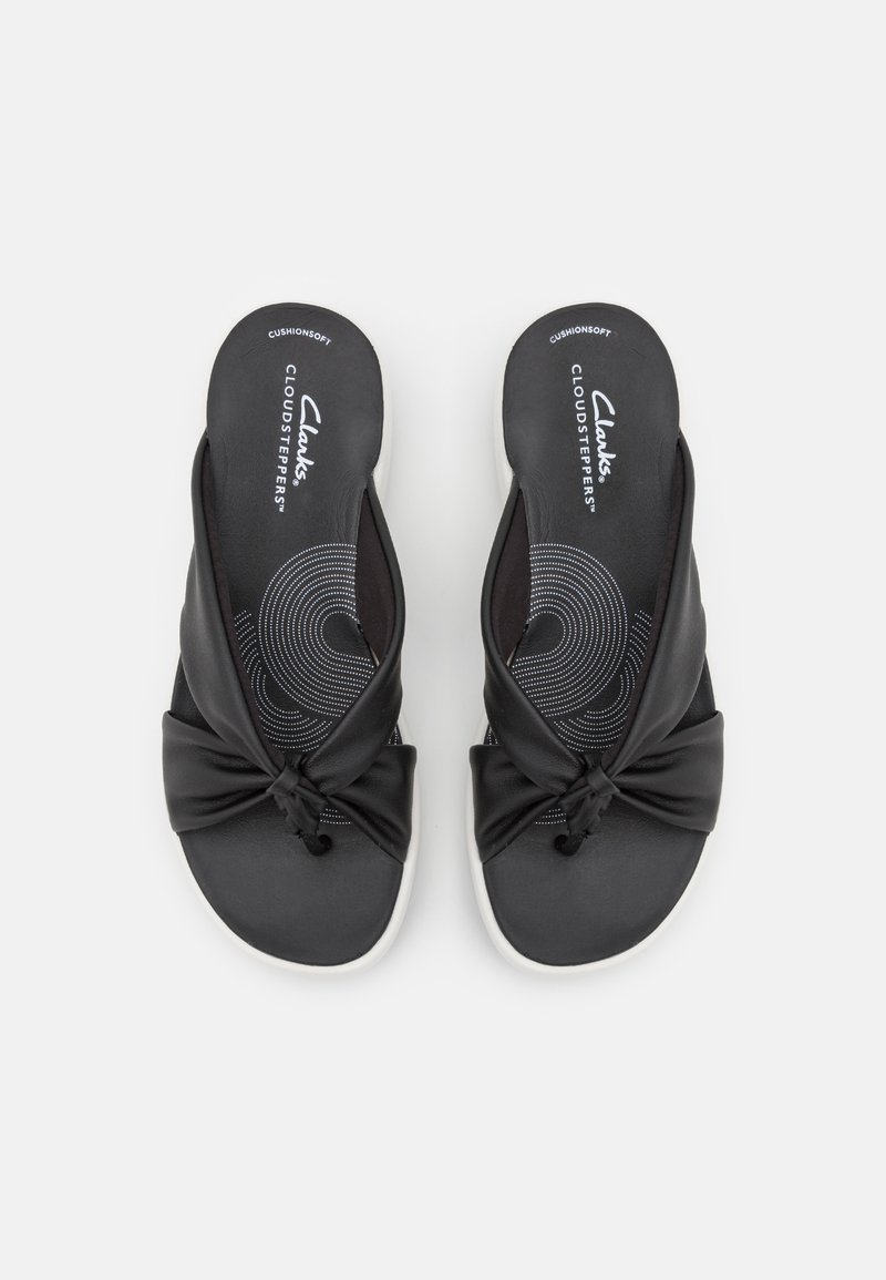 Chanclas negras de material sintético suave, con un diseño anudado en la parte superior y una suela blanca con una plantilla estampada.