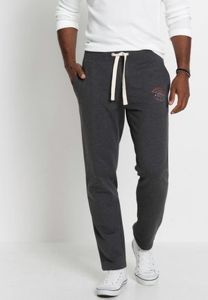 Graue Jogginghose mit einem Kordelzugbund, die ein Logo-Print am Oberschenkel und Seitentaschen hat, kombiniert mit weißen Sneakern.