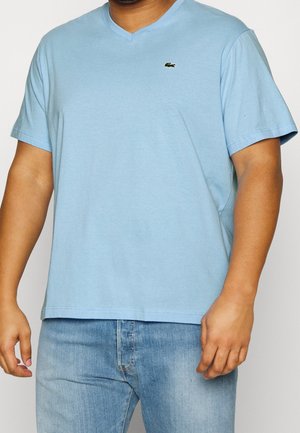 Jasnoniebieska bawełniana koszulka z dekoltem w serek, krótkimi rękawami i małym haftowanym logo na piersi. Gładka tekstura i luźny fason.