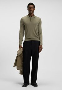 Olivegrünes Langarm-Polohemd, enganliegendes Design mit Kragen und Dreiknopf-Leiste, kombiniert mit schwarzen weit geschnittenen Hosen.