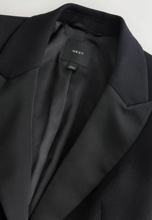 Schwarzer Blazer mit einem glatten Satinfutter, Reverskragen und einem eingewebten Etikett innen. Der Stoff wirkt strukturiert und maßgeschneidert.