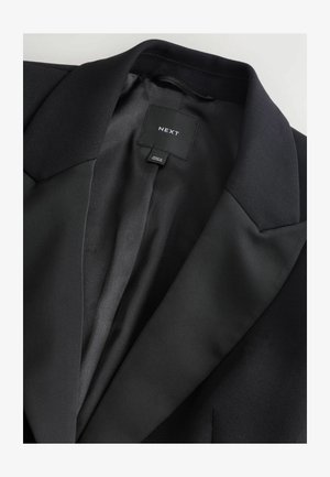 Schwarzer Blazer mit einem glatten Satinfutter, Reverskragen und einem eingewebten Etikett innen. Der Stoff wirkt strukturiert und maßgeschneidert.