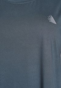 T-shirt corto blu scuro in tessuto testurizzato, con un piccolo logo geometrico bianco sul lato sinistro del petto.