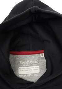 Svart hoodie med ett grått innerfoder. Taggen säger "Band of Rascals", med skötselråd, 100% ekologisk bomull och en röd detalj.