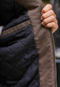 Quilted navy interior fabric, with a smooth brown lining and zipper closure, held by a hand showcasing contrasting textures.