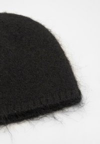 Čierna pletená čiapka vyrobená z mäkkého, chlpatého materiálu. Má rebrovaný okraj a viditeľné vlákna, ktoré vytvárajú textúrovaný vzhľad.