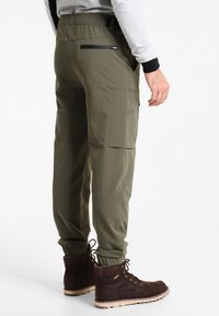 Olijfgroene cargobroek met een elastische tailleband, taps toelopende boorden en zijzakken. Draagt bij bruine wandelschoenen met oogjes.