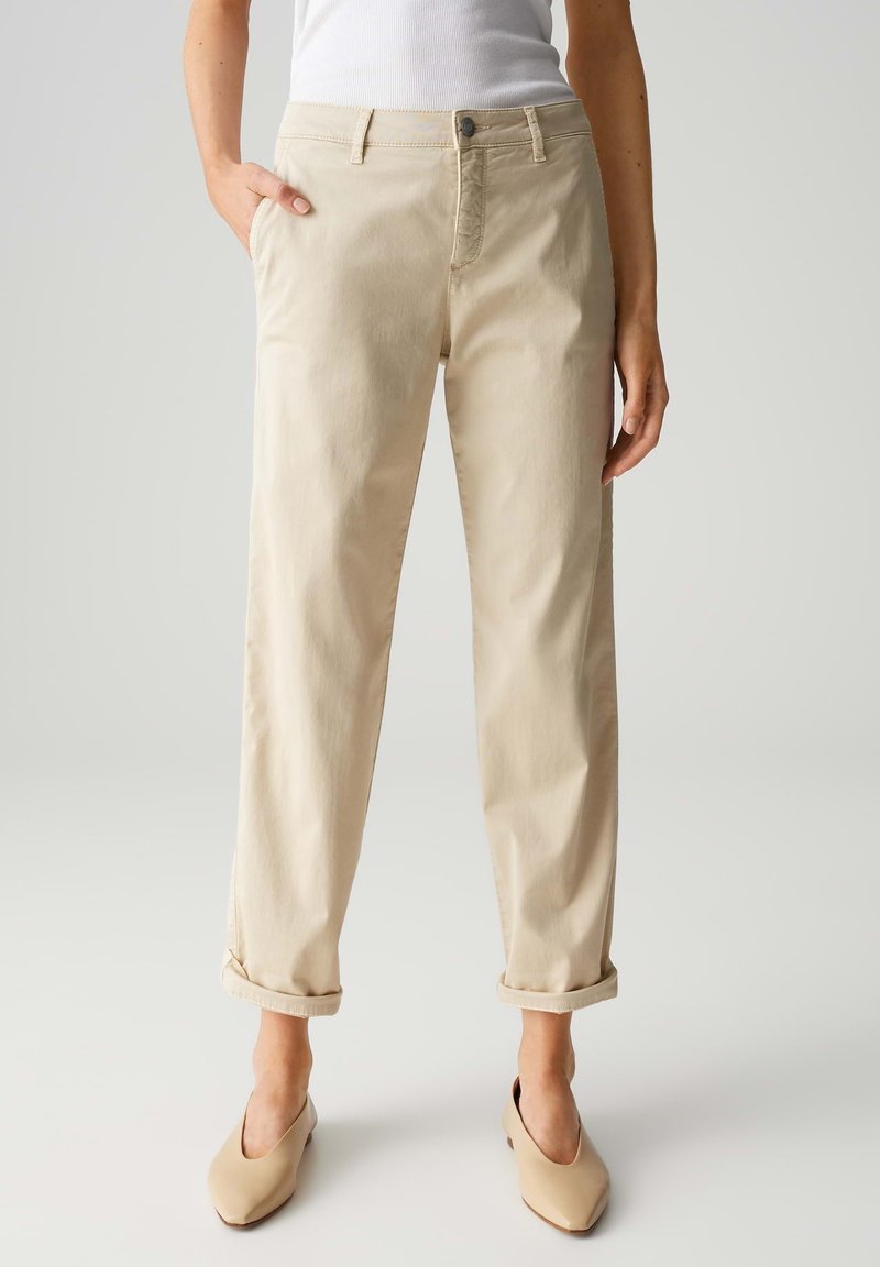 Beige Baumwollhose mit entspannter Passform, ausgestattet mit Gesäßtaschen, umgeschlagenen Säumen und einem Knopfverschluss, kombiniert mit beige-farbenen Slippern.
