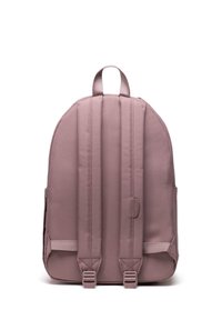 Pink fabric backpack with a rounded shape, padded back, adjustable straps, and two side pockets. Features a minimalistic design and soft texture.