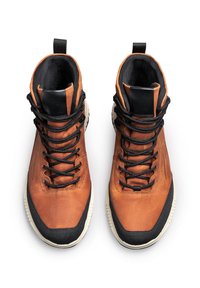 Chaussures montantes en cuir marron avec des garnitures noires, présentant une surface texturée, des lacets noirs et une semelle en caoutchouc blanc.