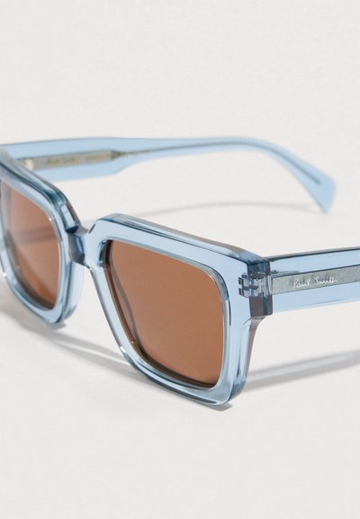 Négyzet alakú napszemüveg világoskék átlátszó kerettel és barna színű lencsékkel. Ezüst színű fém alkatrészek "Paul Smith" gravírozással.