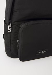 Zwarte rugzak met een gladde, matte textuur, voorzien van een groot hoofdcompartiment en een voorste ritsvak. Inclusief zilverkleurige hardware accentueringen.
