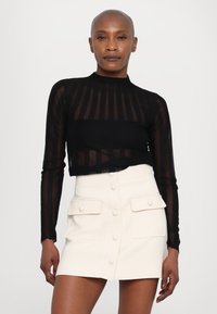 Zwarte, lange mouwen, doorschijnende top met verticale strepen, gecombineerd met een hoogtezijdige, crèmekleurige A-lijn minirok met knoop- en zakdetails.