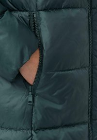 Ciemnozielona kurtka puchowa z zamkiem błyskawicznym, posiadająca widoczne otwarcie kieszeni i pikowaną fakturę. Tkanina wydaje się gładka i błyszcząca.