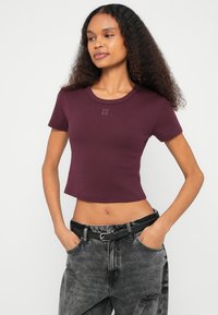 T-shirt cropped bordeaux com decote redondo e mangas curtas, apresentando um pequeno logótipo "HUGO" bordado no peito.