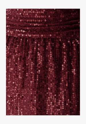 Burgundijas krāsas pērļu audums ar strukturētu virsmu, kurā ir cieši iestrādātas apaļas pērles, kas atstaro gaismu dažādās nokrāsās.
