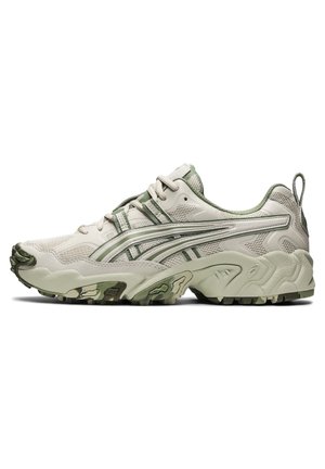 Beżowy i oliwkowo zielony but sportowy z siateczkową i syntetyczną cholewką, wyściełanym kołnierzem, sznurowaniem z przodu, masywną podeszwą i wzorem bieżnika.