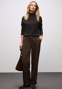 Schwarzer Rollkragenpullover, braune gemusterte weite Hose, passende Handtasche und braune Ankle-Boots. Schlichtes und elegantes Design.