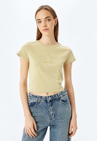 Lys grøn cropped t-shirt med rund hals og korte ærmer, med en broderet stjernedesign i midten.