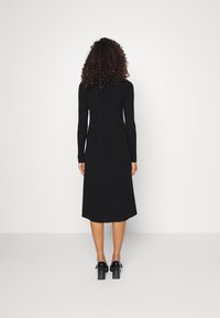 Robe midi noire côtelée à manches longues, avec un corsage ajusté et un ourlet légèrement évasé, associée à des chaussures à talons carrés noires.