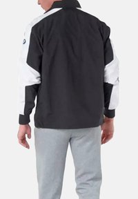 Chaqueta en blanco y negro con un diseño deportivo, que presenta un cuello alto, paneles en contraste y un logo de marca en el hombro izquierdo.