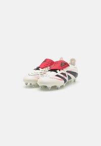 Football boots featuring a white synthetic upper with red and black accents, textured surface, and multiple studs on the sole for traction.