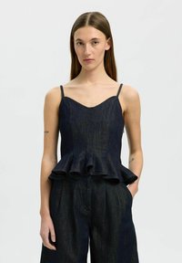 Tmavě modrý peplum top s tenk�ými ramínky, výstřihem do srdce a volánovým lemem, v kombinaci s kalhotami s širšími nohavicemi ze stejného tmavého denimu.