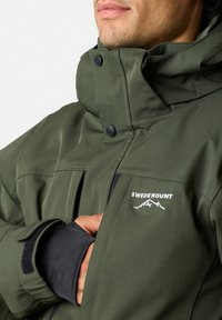 Zielona izolowana kurtka z wysokim kołnierzem, mankietami na rzepy i czarnymi akcentami. Posiada białe logo "SWEDEMOUNT". Wykonana z trwałego materiału syntetycznego.