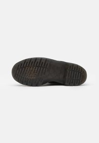 Suela de zapato de goma negra con un patrón de agarre texturizado y surcos profundos, presentando un borde liso y una impresión de logotipo cerca del talón.