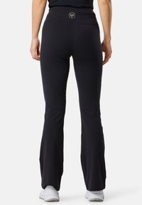 Pantaloni da allenamento neri svasati con una texture liscia, vita alta con un logo dorato e una vestibilità aderente attraverso le cosce, che si allarga in fondo.