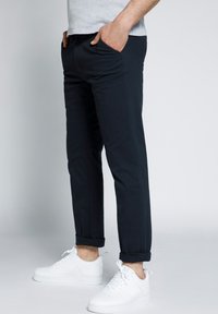 Chinos in cotone blu navy, con una vestibilità slim, dotati di tasche laterali e risvolti, abbinati a sneakers bianche. Design semplice e pulito.