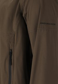 Veste imperméable marron avec une texture lisse, dotée d'une poche zippée et d'un marquage "ENDURANCE" sur la manche.
