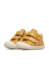 Kindergrößige, beigefarbene Sneaker mit weißen Sohlen, doppelten Klettverschlüssen und bedruckten Sportbällen, darunter Fußball, Basketball und American Football.