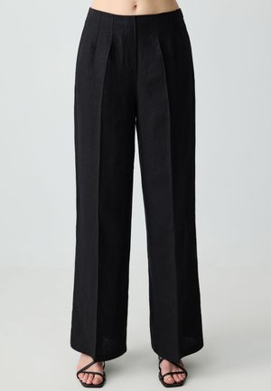 Pantalons larges en lin noir avec des plis à l'avant, une taille haute et des poches latérales. Texture lisse, design long jusqu'au sol et esthétique minimaliste.