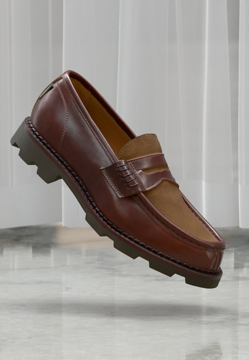 Brown leather loafer with thick rubber sole and suede upper section, set against a marble floor and sheer white curtain background.