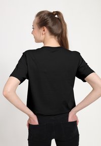 Czarny t-shirt z krótkim rękawem i okrągłym dekoltem, wykonany z bawełny, pokazany od tyłu, z gładką teksturą i luźnym krojem, zestawiony z czarnymi dżinsami.