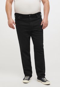 Jeans de denim negro con un diseño de pierna recta, que cuentan con una cintura de altura media, bolsillos frontales y costuras en contraste, combinados con zapatillas negras.