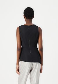 Top nero senza maniche con chiusura a zip sulla schiena, caratterizzato da un design peplum. La modella lo ha abbinato a pantaloni d'argento lucenti.