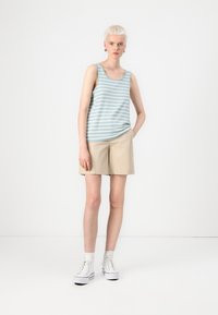 Lichtblauw gestreept tanktop met een ronde halslijn, gecombineerd met beige shorts. Model draagt witte hoge sneakers.