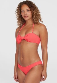 Koraal kleurige bikini set met een bandeau top met knoopdetails en verstelbare bandjes, in combinatie met bijpassende aansluitende broekjes. Gelaagd stof.