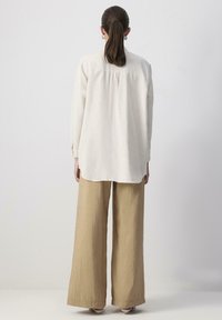 White linen long-sleeve shirt with a loose fit, back pleat, and buttons at the cuffs, paired with light beige wide-leg trousers.