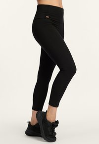 Zwarte leggings met een hoge tailleband, gemaakt van zachte, rekbare stof. Heeft een kleine logo-accent nabij de tailleband.