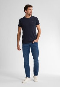 Camiseta de cuello redondo en azul marino con mangas cortas, combinada con unos vaqueros azules y zapatillas deportivas blancas. Diseño simple, sin patrones ni acentos.