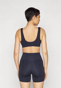 Jūras spēku sporta krūšturis ar platām siksnām un noapaļotu aizmuguri, kopā ar atbilstošām augsto vidukli šortiem, kas izceļas ar gludu tekstūru un smalku zīmolu.