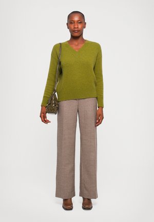 Green knitted sweater with V-neck, paired with brown and white plaid wide-leg trousers. Accessory: small textured handbag. Brown footwear.